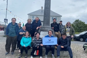 Ireland Program Students in front of a Celtic Cross one holding a small banner that says Landmark College