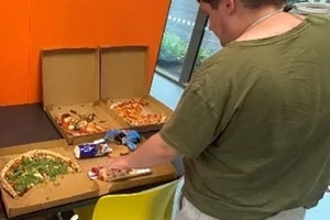 Jack standing in front of pizzas in pizza boxes grabbing a slice