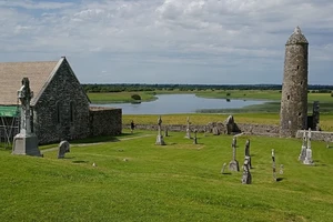 Northern Round Tower at Clonmacnoise overlooking the Shannon river, Celtic crosses in the foreground.
