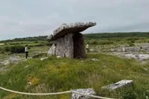 Megalithic Dolmen in a grassy field surrounded by a rope perimeter bordered by flat rock formations