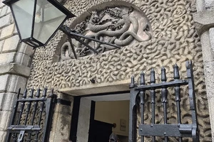 Stone carving of serpents entwined over the entrance to Kilmainham Gaol with a Landmark student entering the building.