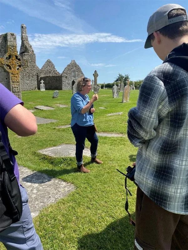 Instructor talking to students about the Cross of the Scriptures, a reproduction of which appears behind and to the left of the group.