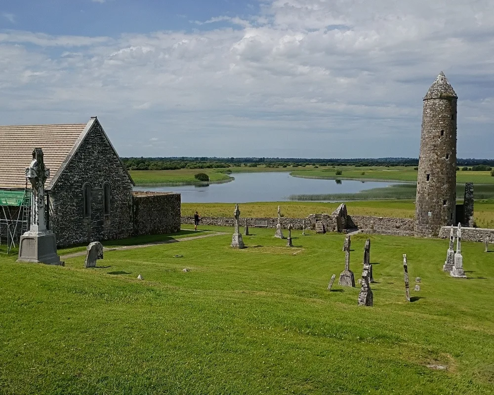 Northern Round Tower at Clonmacnoise overlooking the Shannon river, Celtic crosses in the foreground