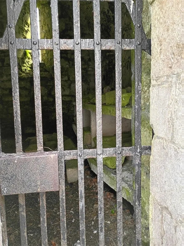 An iron gate framed in stone looking into an interior of mossy green stonework