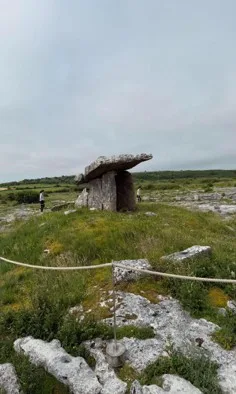 Megalithic Dolmen in a grassy field surrounded by a rope perimeter bordered by flat rock formations