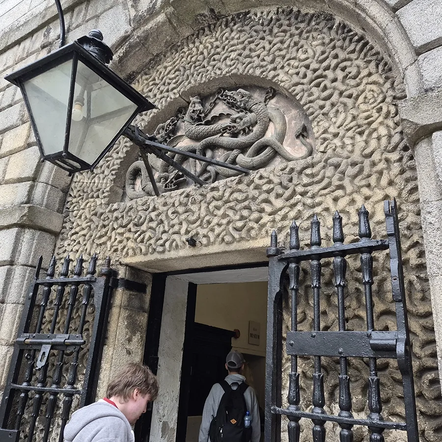 Stone carving of serpents entwined over the entrance to Kilmainham Gaol with a Landmark student entering the building.