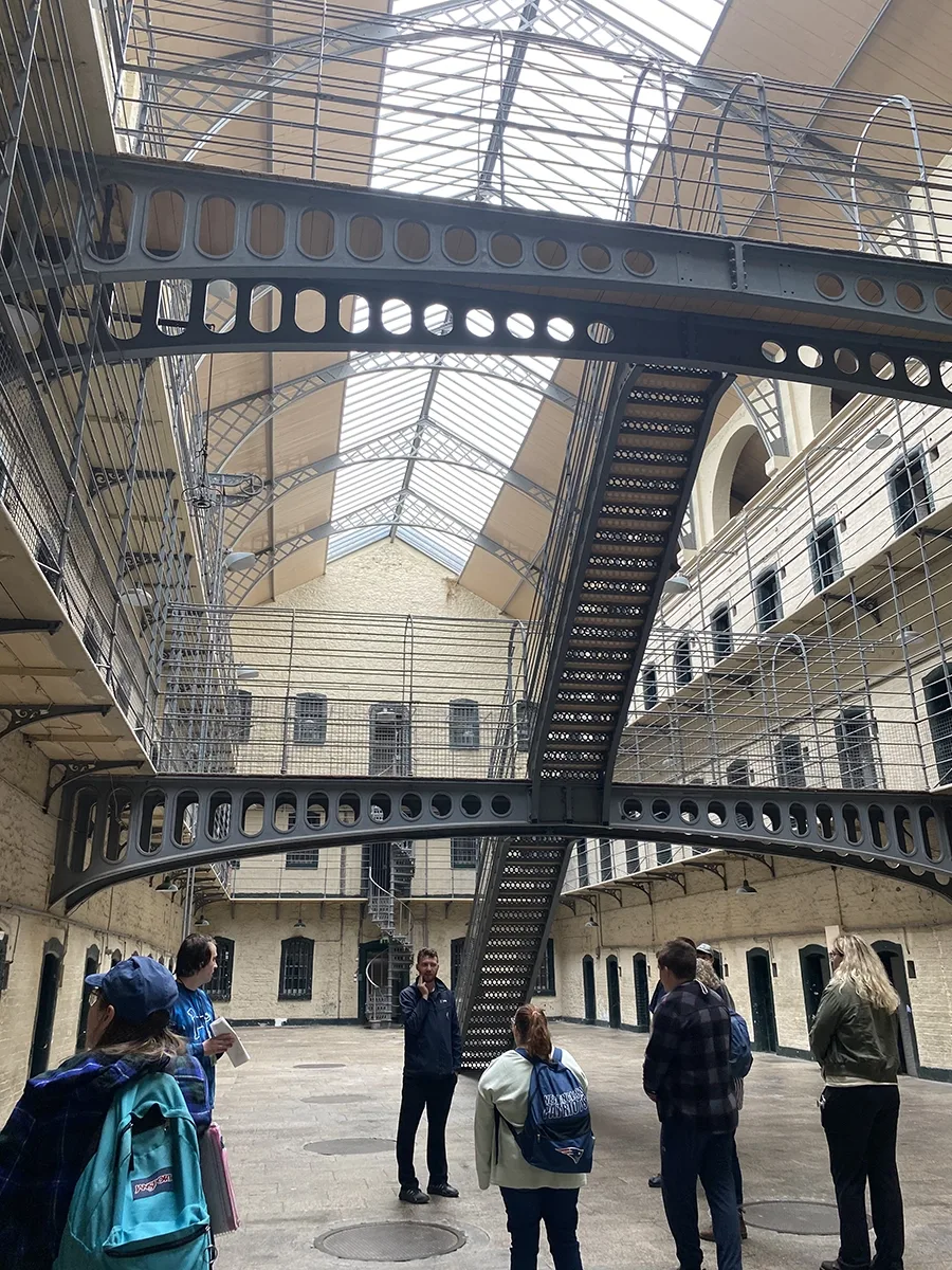 students listening to tour guide and looking up at the 3 level prison structure designed as a panopticon.