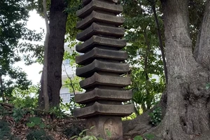 A tall, multi-tiered stone structure stands among trees in a garden.
