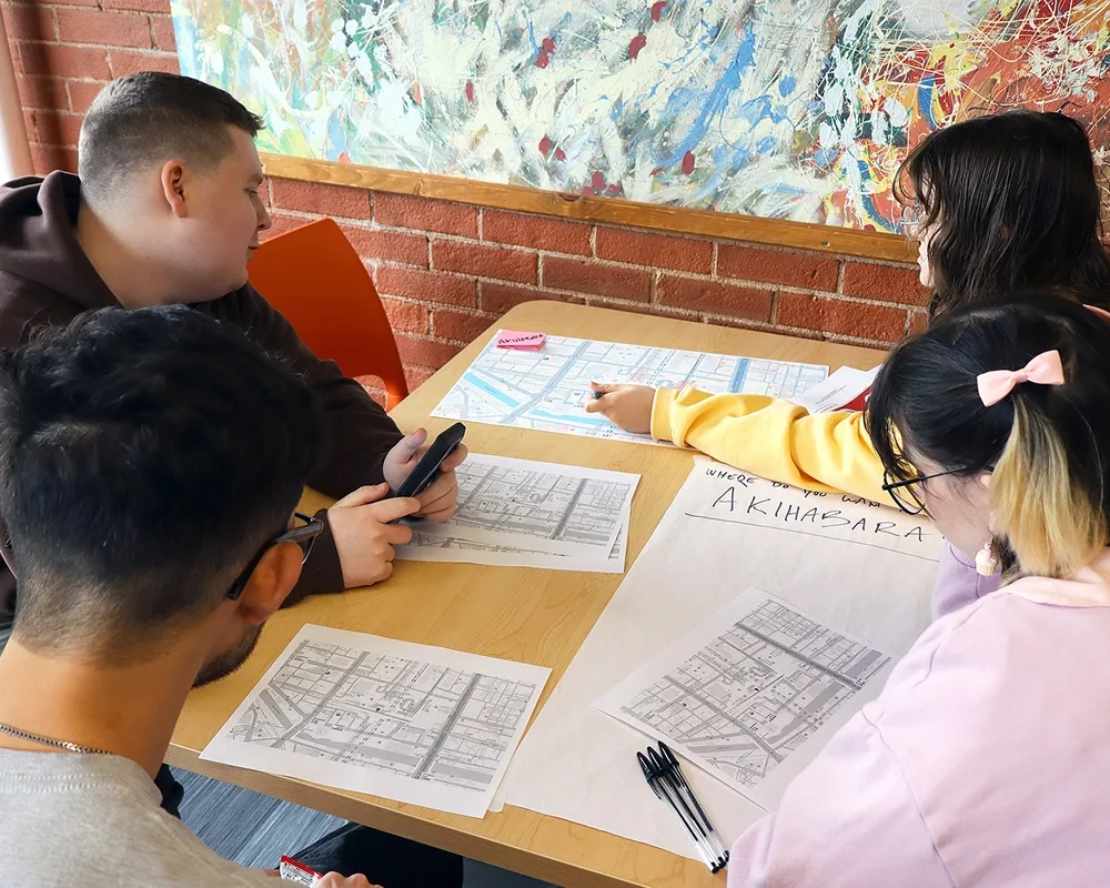 A photo of a small group of four students looking at maps of Tokyo and using a smartphone. 