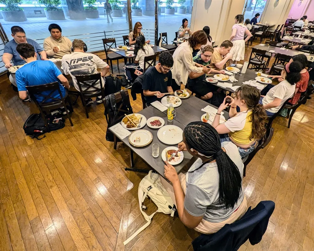 College students sit at tables in groups of four, eating lunch.