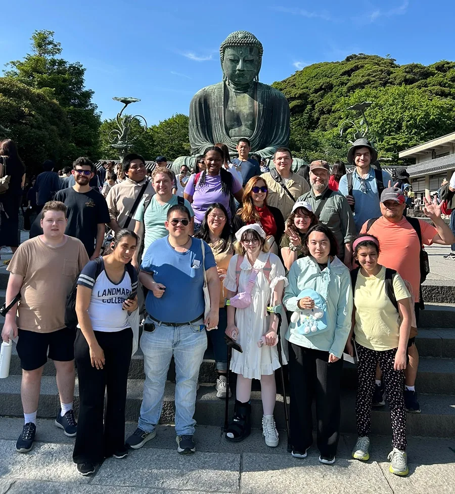A group of students and group leaders pose for a photo in front of an enormous Buddha statue.