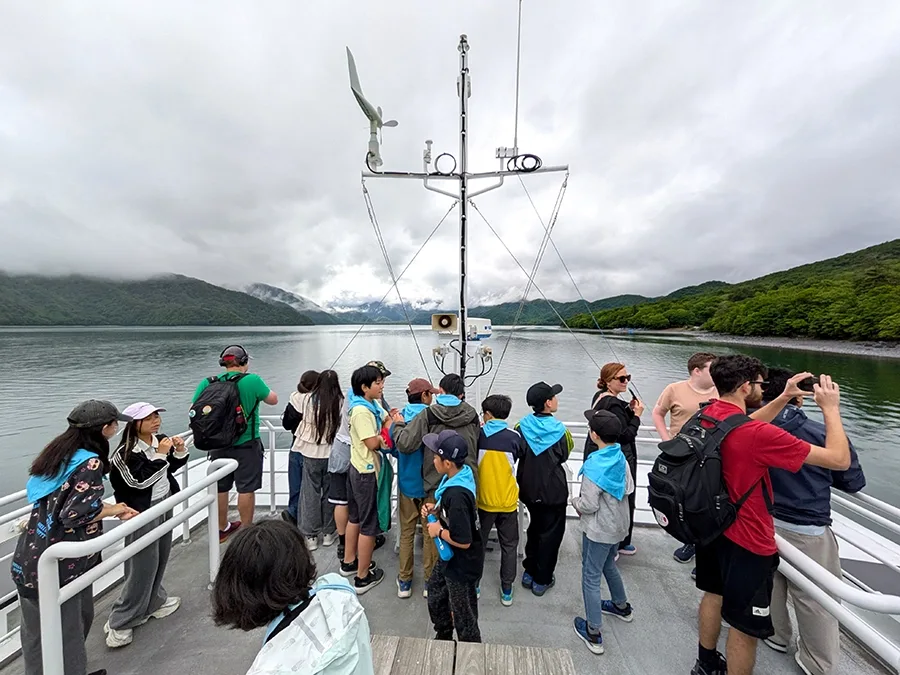 The view from the top deck of a small ferry-size cruise ship. People are looking at clouds, mountains and water.