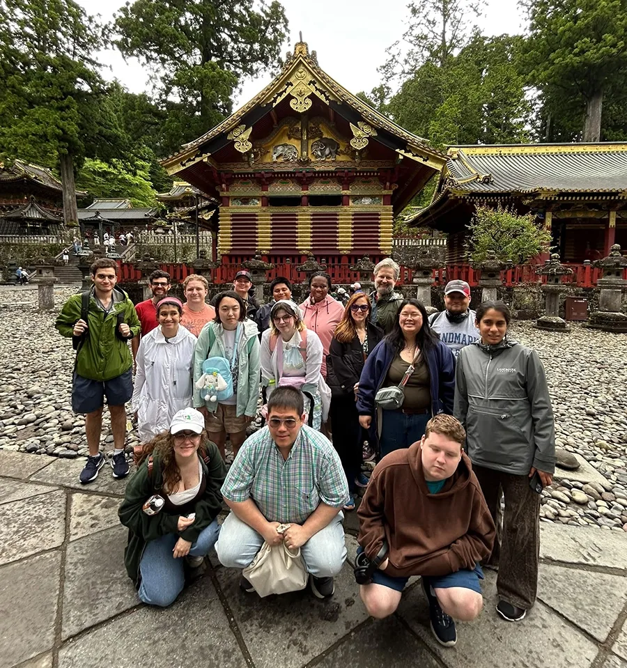 A group poses for a photo in front of an elaborate Buddhist shrine building.