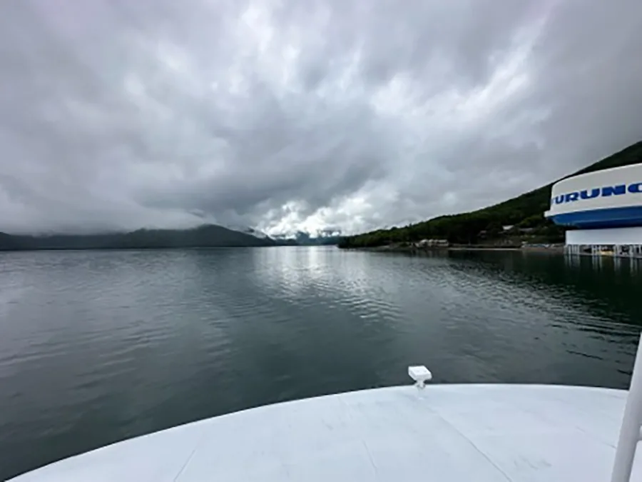 The view from atop a cruise around a lake. Water, buildings, mountains, and clouds are visible.