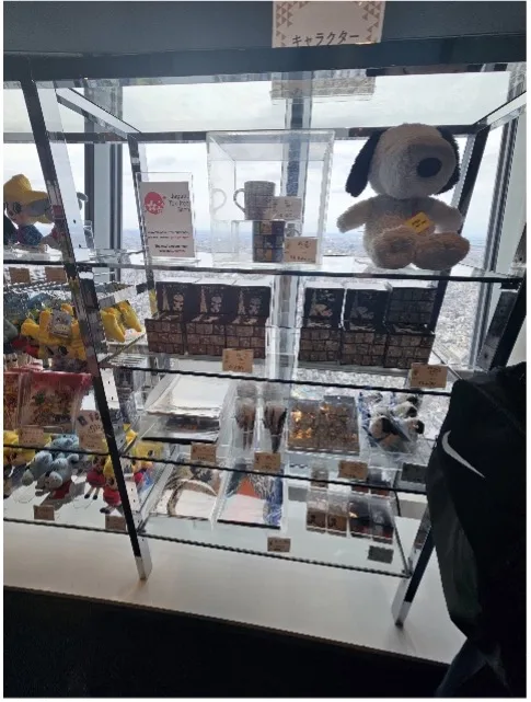 A shelf featuring Snoopy-themed plush dolls, cups, and other souvenirs.