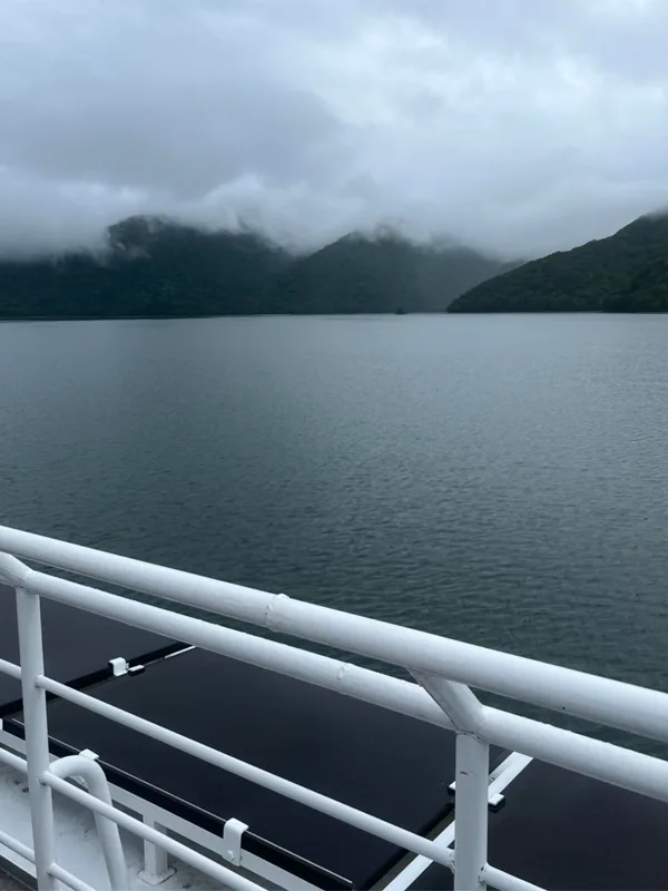 The view from atop a boat looking out at water, hills, and clouds.