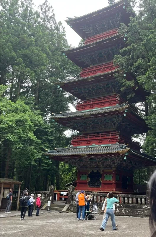 A five-storied pagoda amongst a wooded setting with tourists about.