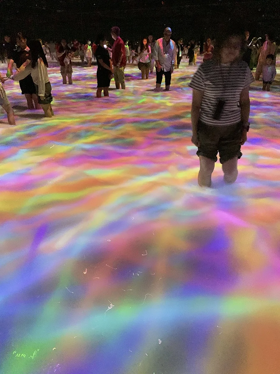 A person stands in near knee-deep water, while blurs of color swirl around them.