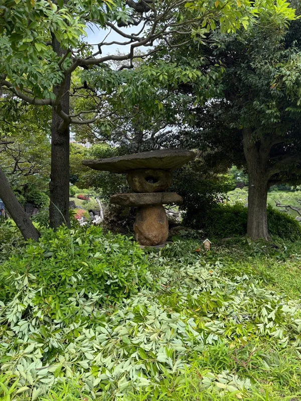 A small balanced stone structure stands among trees in a garden.