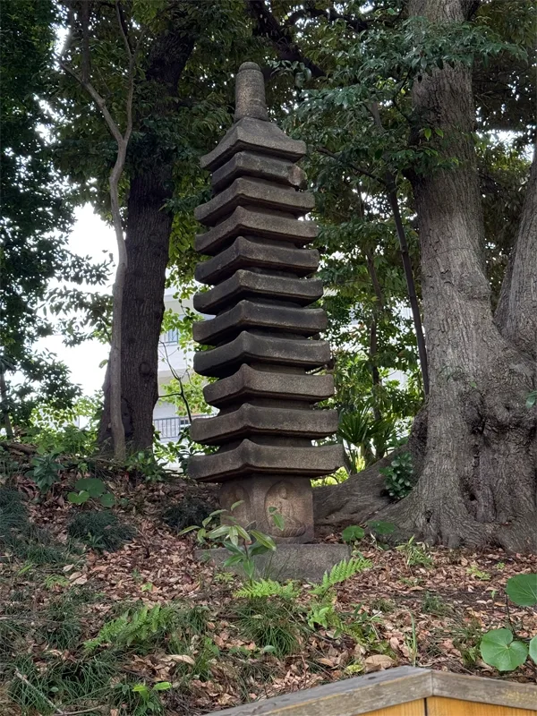 A tall, multi-tiered stone structure stands among trees in a garden.