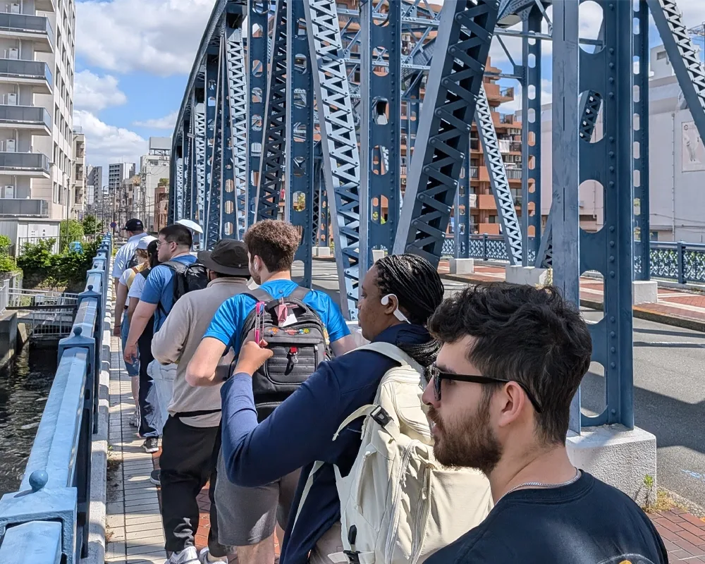 College students walk single-file across a steel bridge.