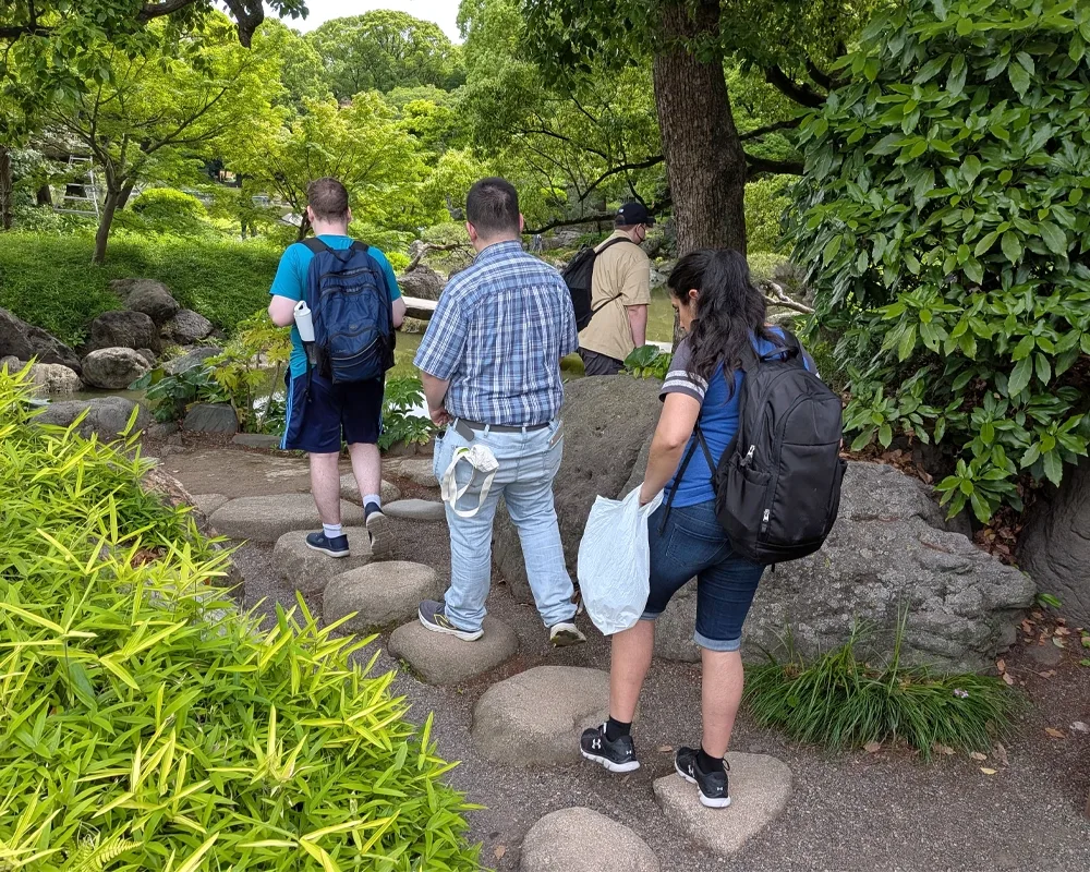 Students walk upon large stones through a Japanese garden.