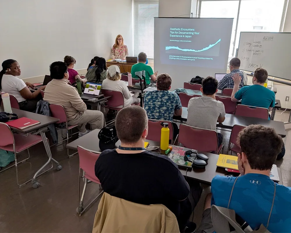 A professor stands at a podium in front of a classroom of students.