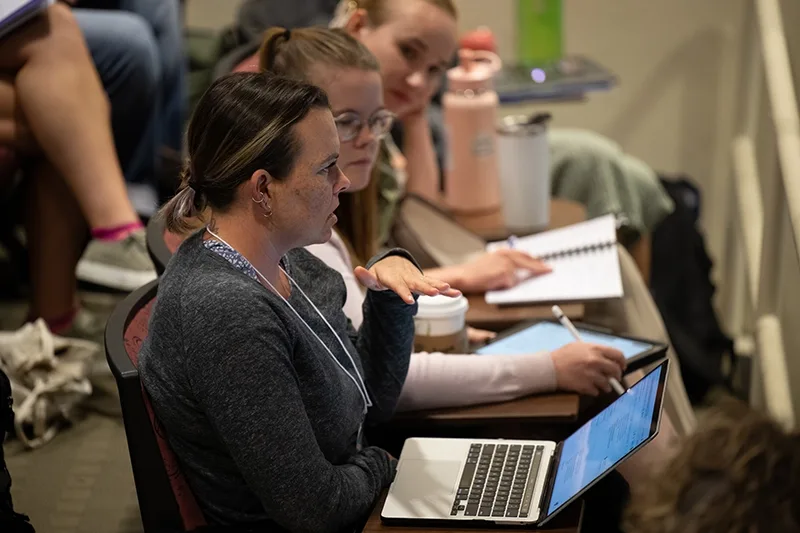 A woman in an audience asking a question with a laptop on front of her