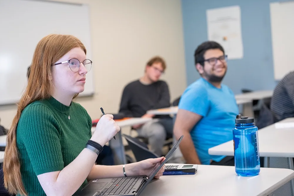 A red-headed girl with glass sitting in class next to a male student with a blue shirt.