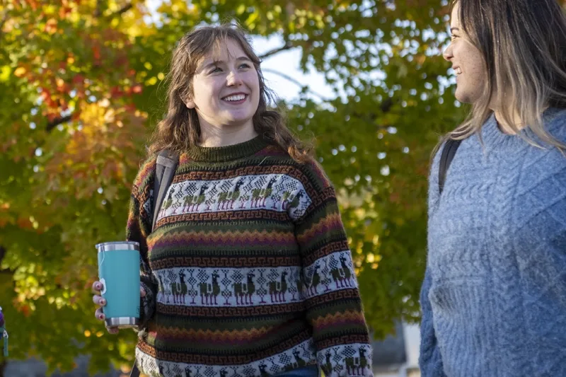 Woman with long brown hair walking outside holding coffee receptacle