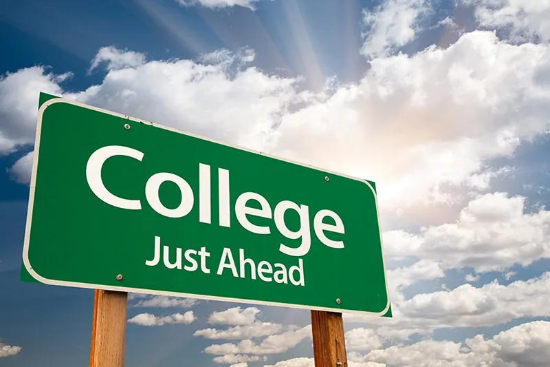 College Just Ahead written on a green road sign with  white clouds in a blue sky.