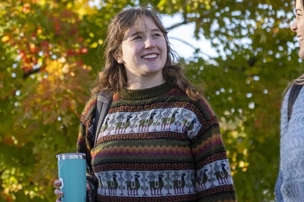 Young woman walking outdoors holding a blue coffee receptacle