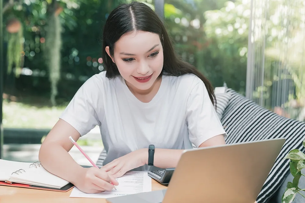 A female student taking notes in front of a laptop computer.