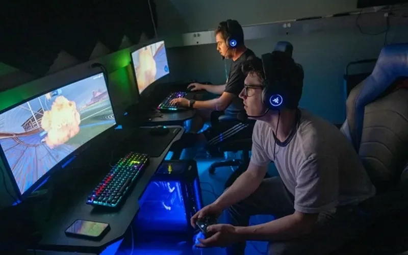 Gamers competing on computer screens in a dimly lit room.