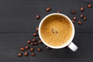 An aerial view of a cup of coffee with coffee beans scattered on a gray wooden surface.