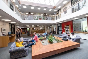 Students sit in comfortable chairs on the first floor of the Landmark College library. Above them is a balcony and a skylight.