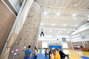 A group of people hangs out and climbs the climbing wall at Landmark College.