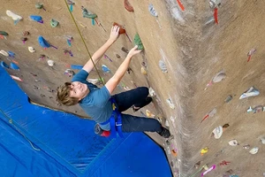 A student scaling the climbing wall in the gym.