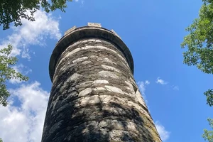 The top of a tower against a blue sky with treetops.