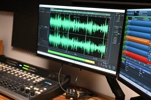Two computer monitors and a soundboard. A software program shows tracks and sound waves.