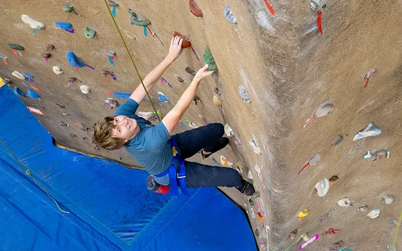A student scaling the climbing wall in the gym.