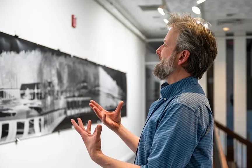 Person gesturing at a black and white photograph in a gallery.