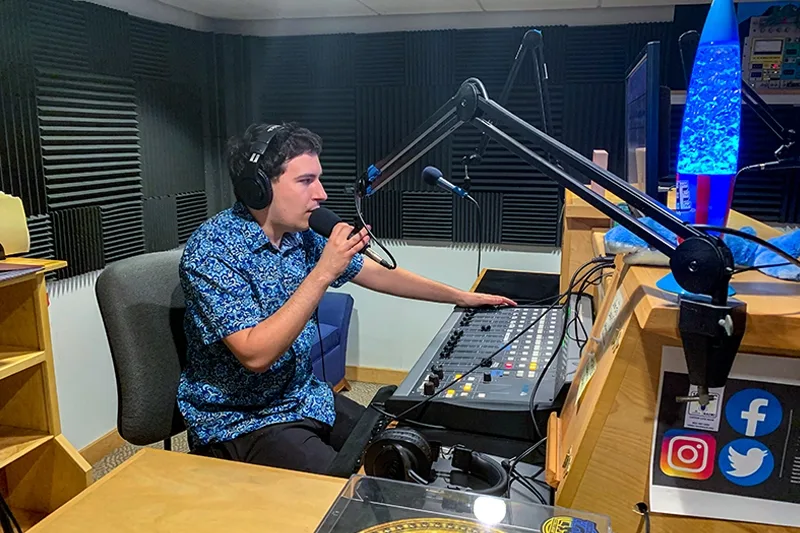A student radio host talking into a microphone in the WLMC studio.