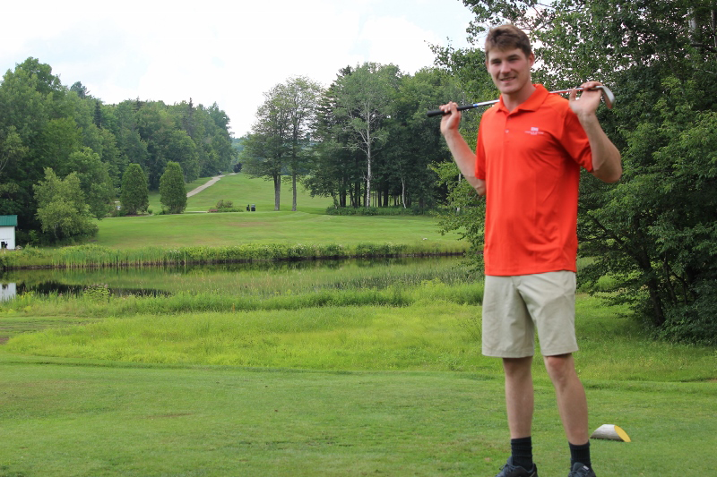 Zachary Zoidis standing on a golf course in an orange shirt holding a club over his shoulders