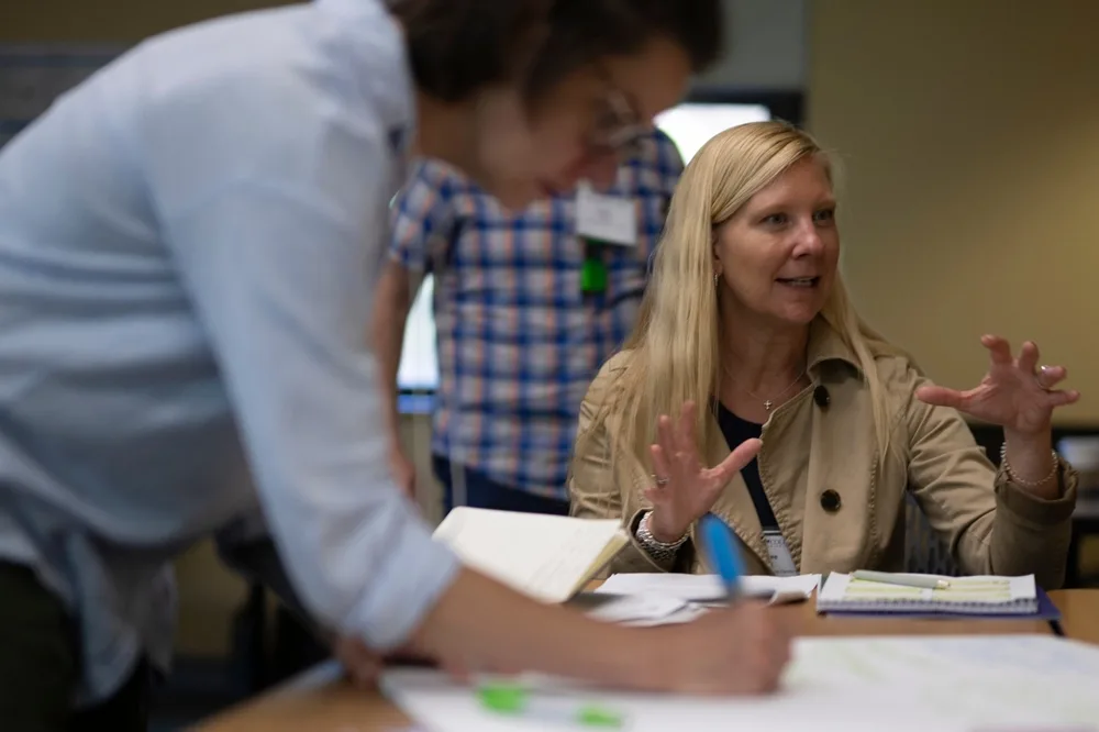 A woman speaking enthusiastically while another writes down something on a large piece of paper.