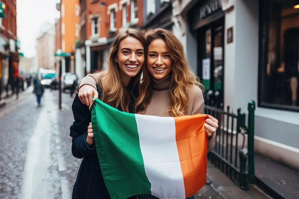 Two female students holding an Irish flag on a cobblestone street.