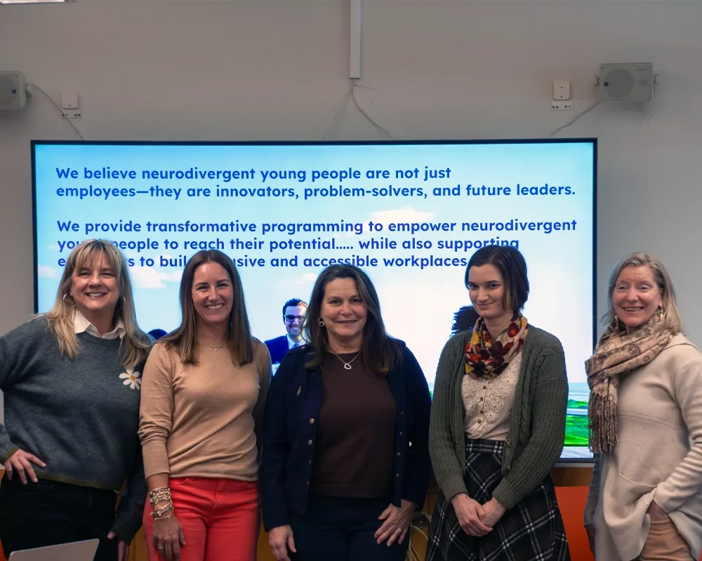 Five women standing in front a video screen dispaying an empowering message for neurodiverse individuals.