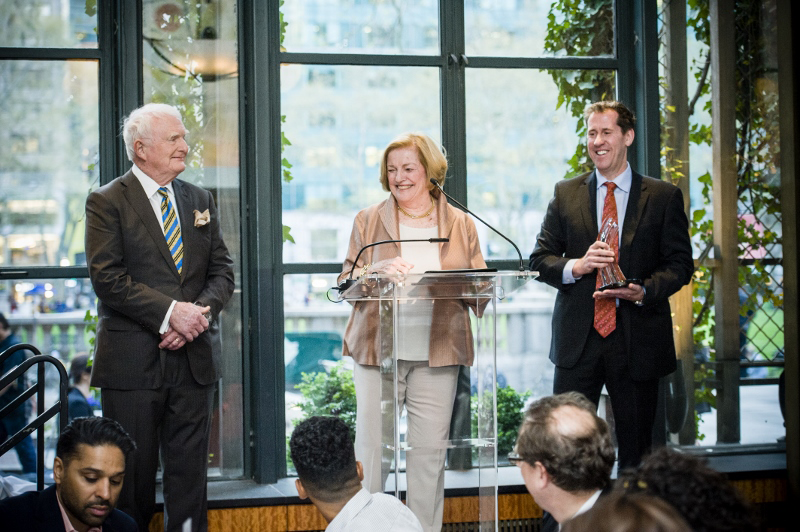 Three people standing at a podium in front of large window at the gala.