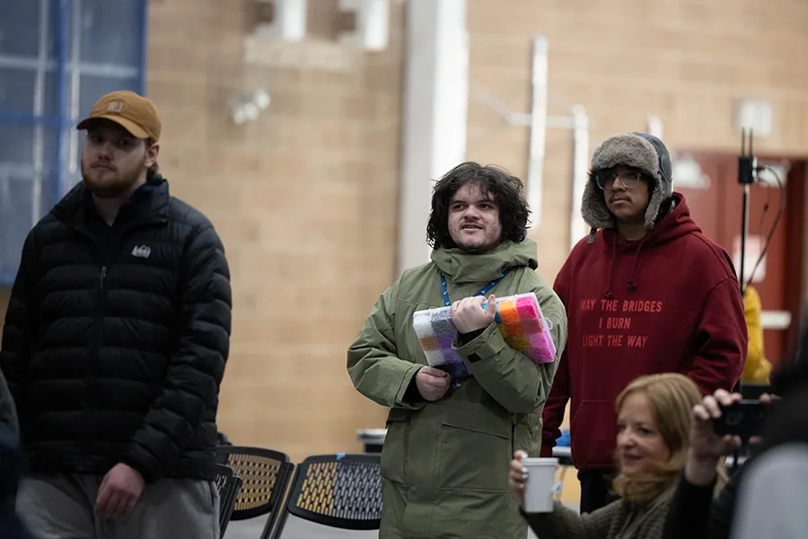 Students stand in line at convocation. The student in the center is carrying a box of brightly colored beading supplies.