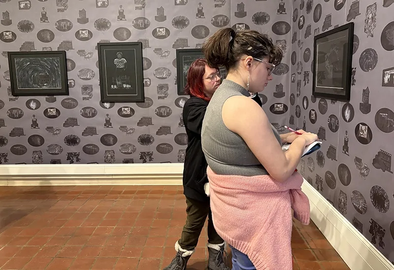 Two students make notes while looking at artwork hanging on a gallery wall